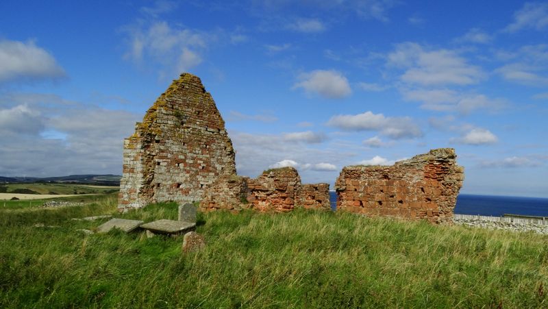 Weathered red sandstone walls of the ruined Old St Helen’s Church standing in grass with the sea beyond.