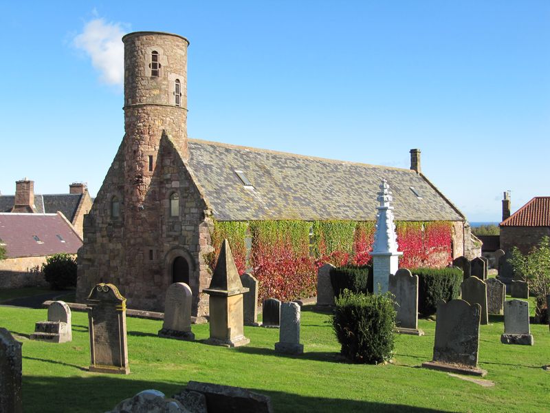 Cockburnspath parish church and its round west tower seen across a graveyard on a clear autumn day.
